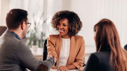 A businesswoman shaking hands with a colleague in a cozy meeting room, finalizing a plan to implement cloud printing solutions to reduce IT costs.