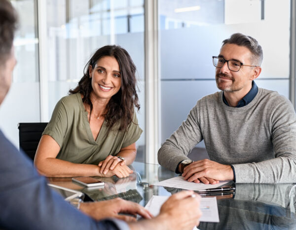 Three professionals are engaged in a discussion sitting around the glass table, collaborating on print management strategies.