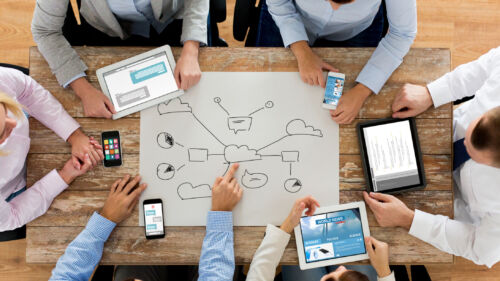 A top-down view of an office team brainstorming around the big sheet of paper displaying a cloud printing diagram.