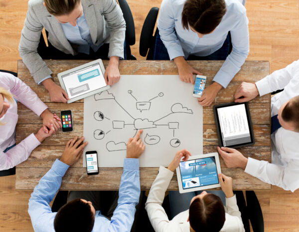 A top-down view of an office team brainstorming around the big sheet of paper displaying a cloud printing diagram.