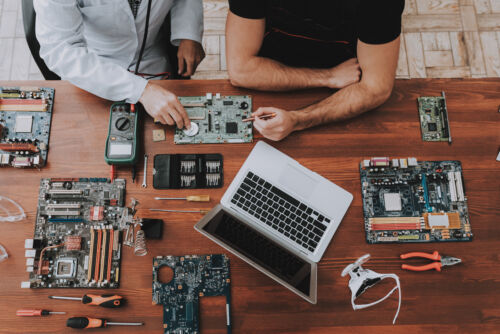 A wooden table with hardware components and tools; two people assembling circuit boards for a setup.