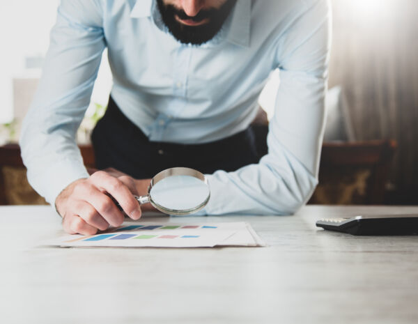 A man in business attire examines a document with a magnifying glass, emphasizing the importance of print knowledge.